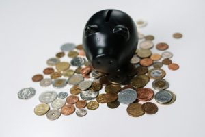bank loans. Black piggy bank surrounded by a variety of coins on a white surface, symbolizing savings and finance.